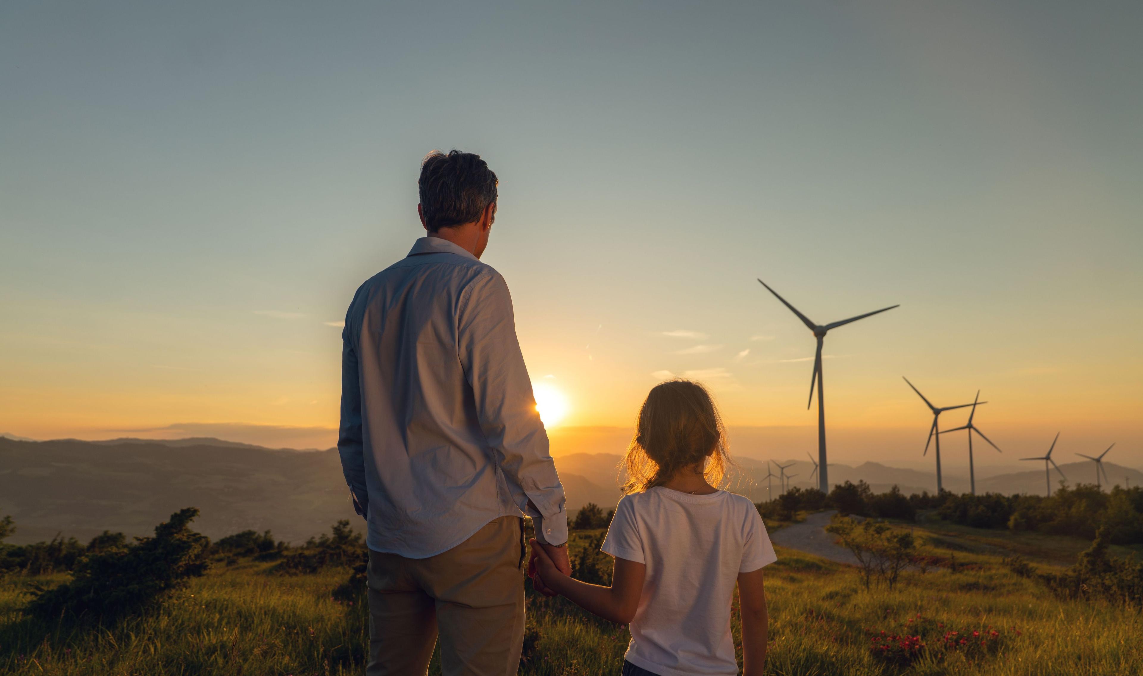 Mann und Kind bei Sonnenuntergang mit Windrädern im Hintergrund