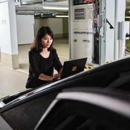 Eine Frau bedient ihren Laptop in der Tiefgarage auf einem Elektroauto