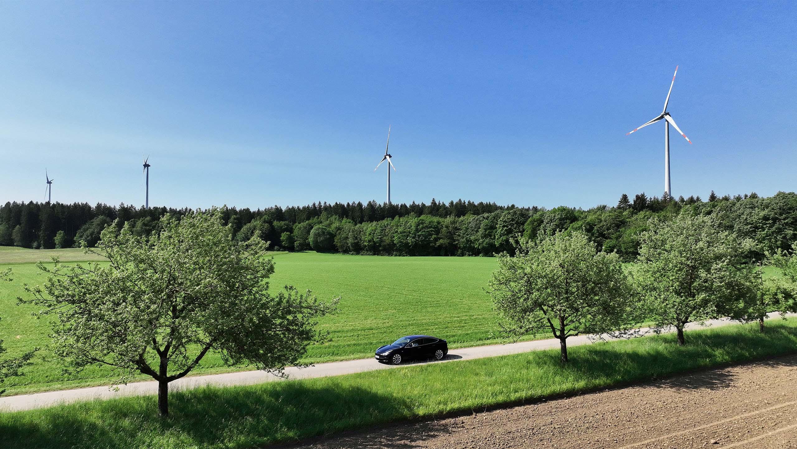 Landschaft mit Elektroauto vor Windraedern