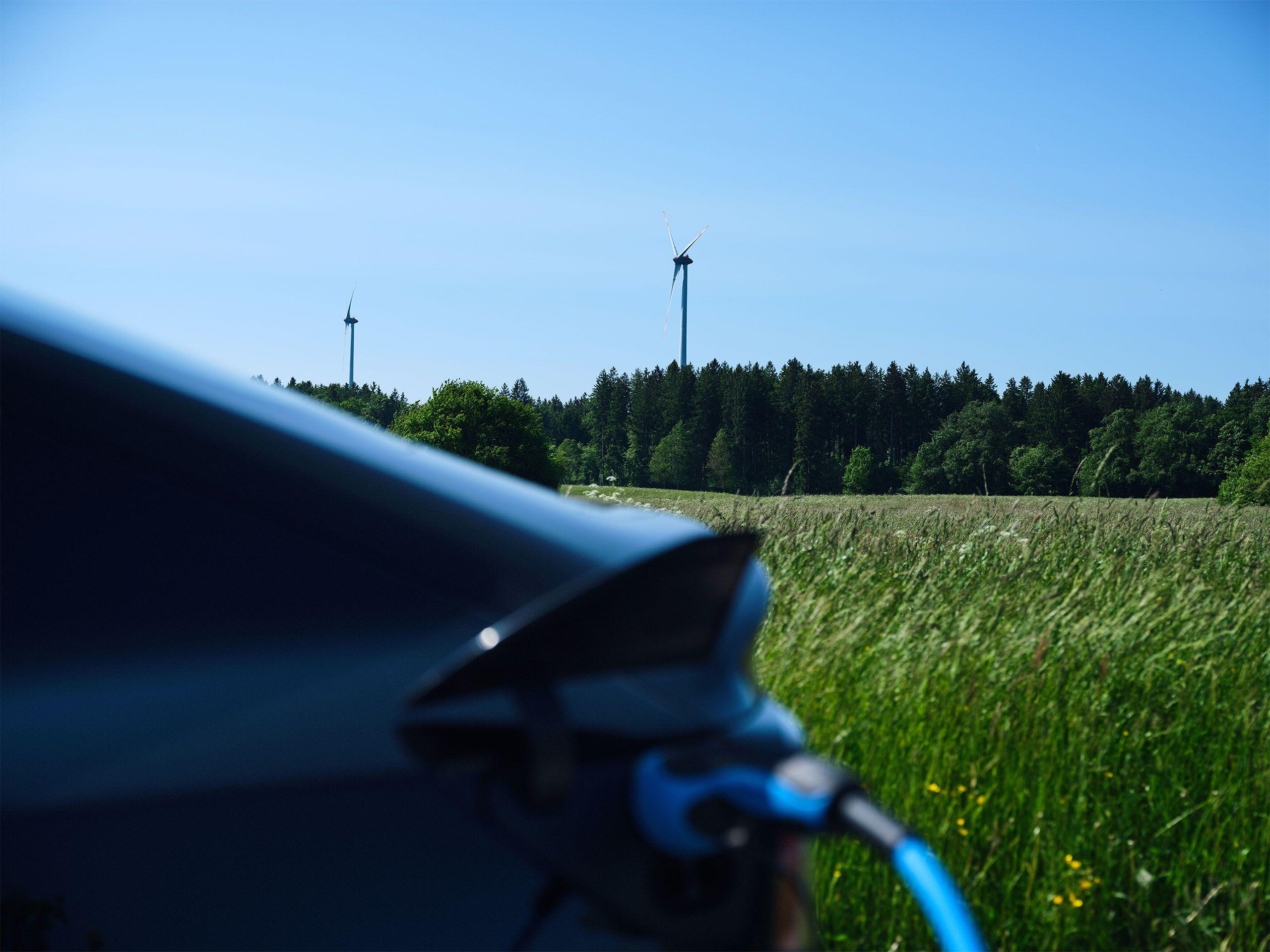Ein Elektroauto lädt vor einer Landschaft mit Windraedern