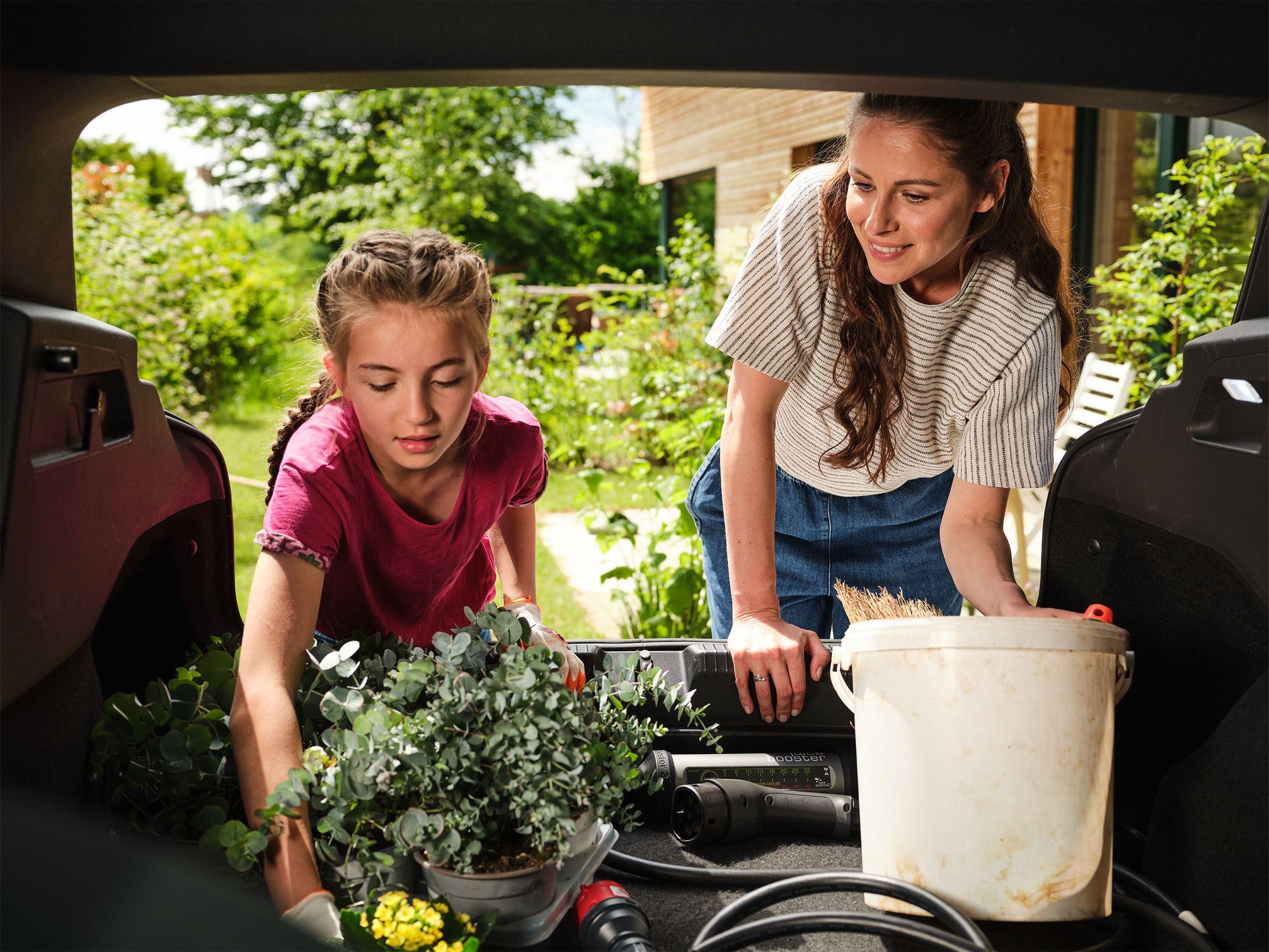 Eine Mutter und ihre Tochter holen Blumen aus dem Kofferraum ihres Elektroautos