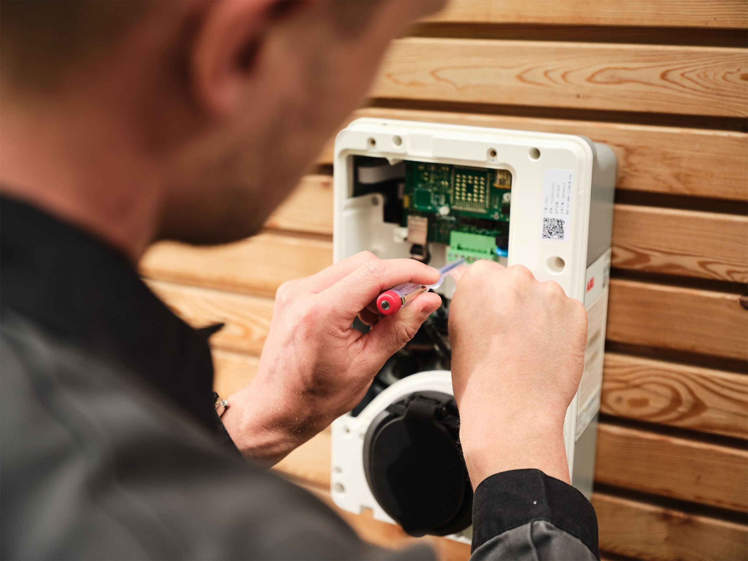 Ein Mann montiert eine Wallbox an ein Holzhaus
